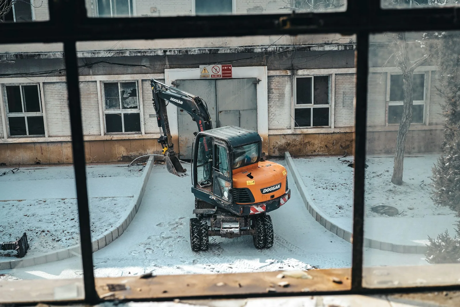 A Doosan-badged wheeled excavator working on a snowy jobsite