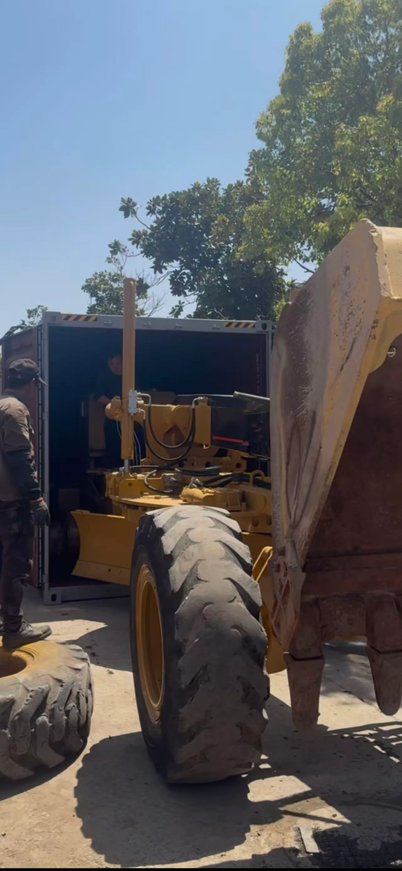Motor grader being loaded into a standard shipping container at the SK yard